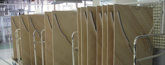 Rows of unfinished piano soundboards on a factory floor, illustrating a stage in the piano manufacturing process.