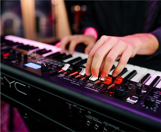 Musician's hands playing a modern synthesizer with various controls and LED indicators, highlighting the versatility of electronic keyboard instruments in the piano industry.