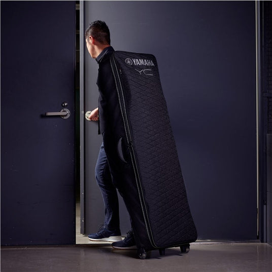 Person carrying a Yamaha keyboard case entering a room.