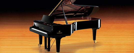 A shiny black grand piano on a polished wooden floor with the lid open, showcasing the strings and interior.