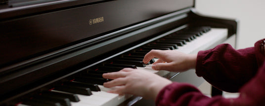 Person playing a Yamaha piano, focusing on the hands and the keyboard.