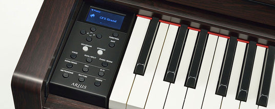 Close-up of a digital piano control panel and part of the keyboard, displaying various function buttons and the screen showing "CFX Grand" on an electronic interface, with the brand name "ARIUS" visible at the bottom.