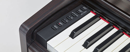 Close-up of a digital piano's control panel beside the keyboard with dark woodgrain finish, white and black keys, and red felt lining above the keys.