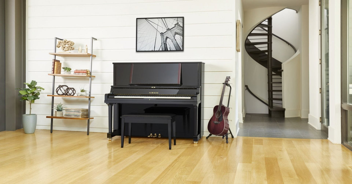 Elegant living room interior with a black upright piano, matching bench, and a classical guitar resting beside it, suggesting a home with a love for music and piano playing.